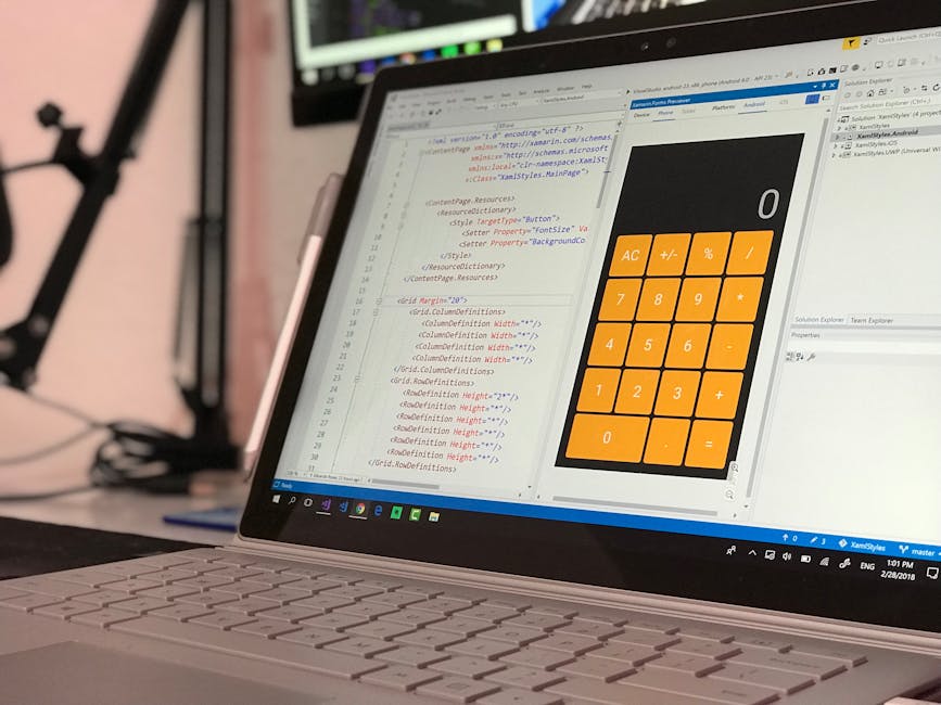 A close-up view of a laptop displaying lines of HTML coding on the left side of the screen, with a large digital calculator interface overlay featuring orange buttons for various functions on the righ